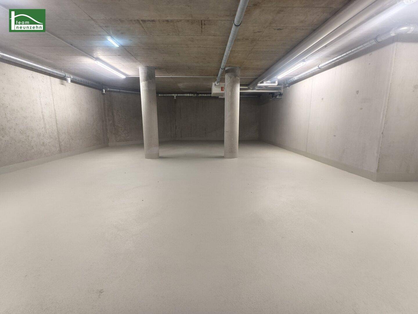 Beton-Kellerbereich mit tragenden Säulen, sichtbaren Rohren und hellen Leuchtstofflampen.