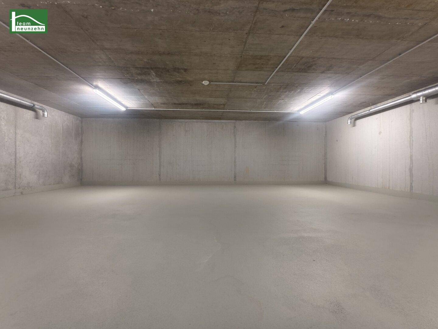 Geräumiger, sauberer Kellerraum mit Betonoberflächen und heller Beleuchtung durch Deckenlampen.