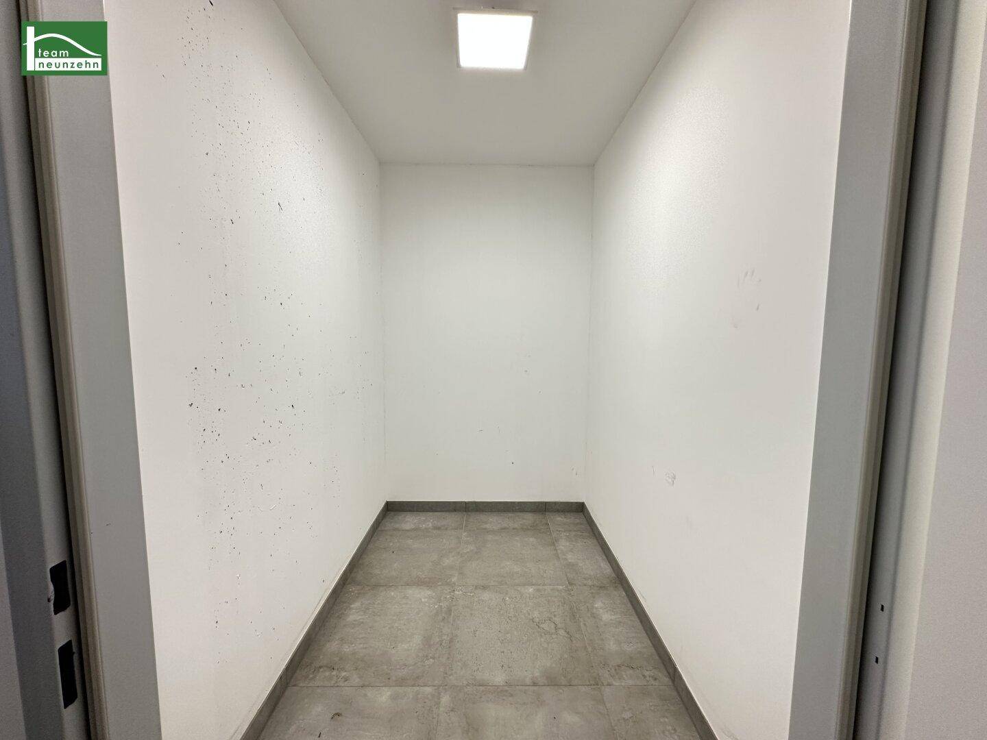 Leerer Abstellraum mit Betonboden und weißen Wänden, ideal für zusätzlichen Stauraum.