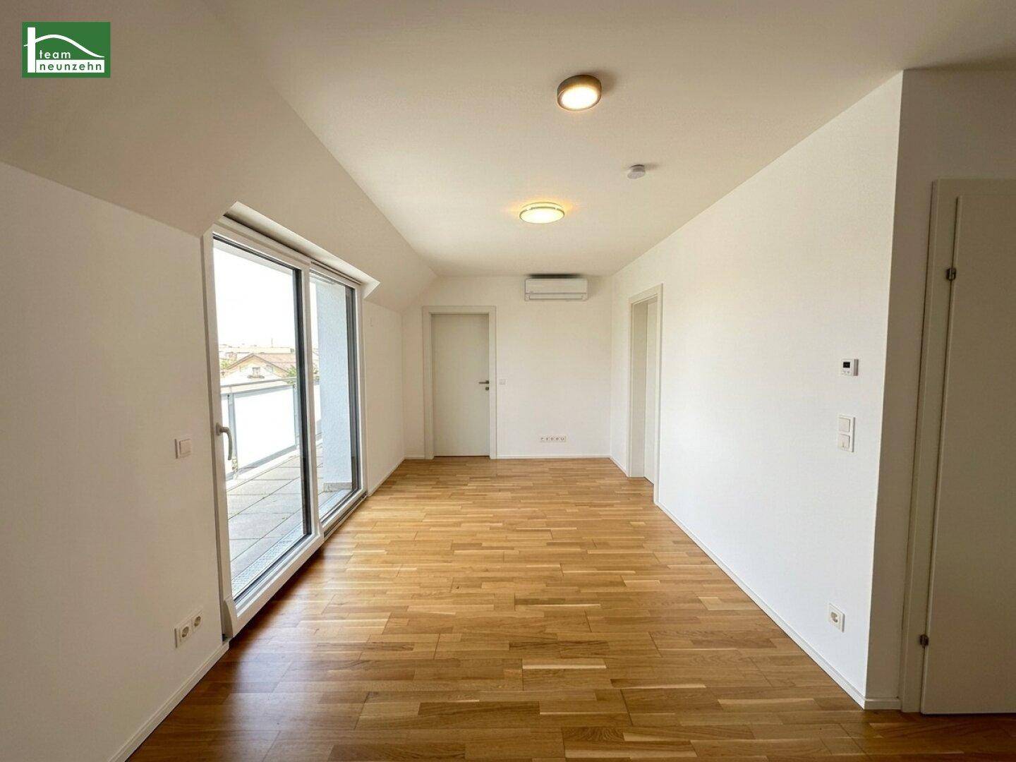 Geräumiger Wohnbereich mit hellem Parkettboden, weißen Wänden und großem Terrassenzugang.