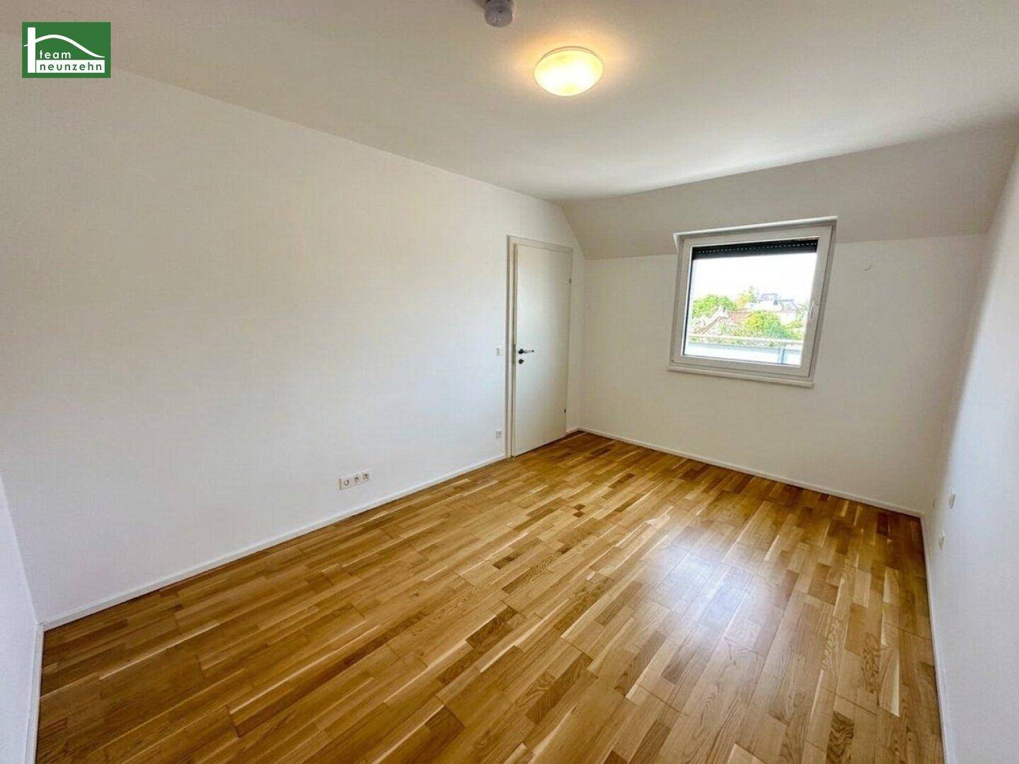 Helles Schlafzimmer mit Parkettboden, weißen Wänden und einem Fenster für Tageslicht.