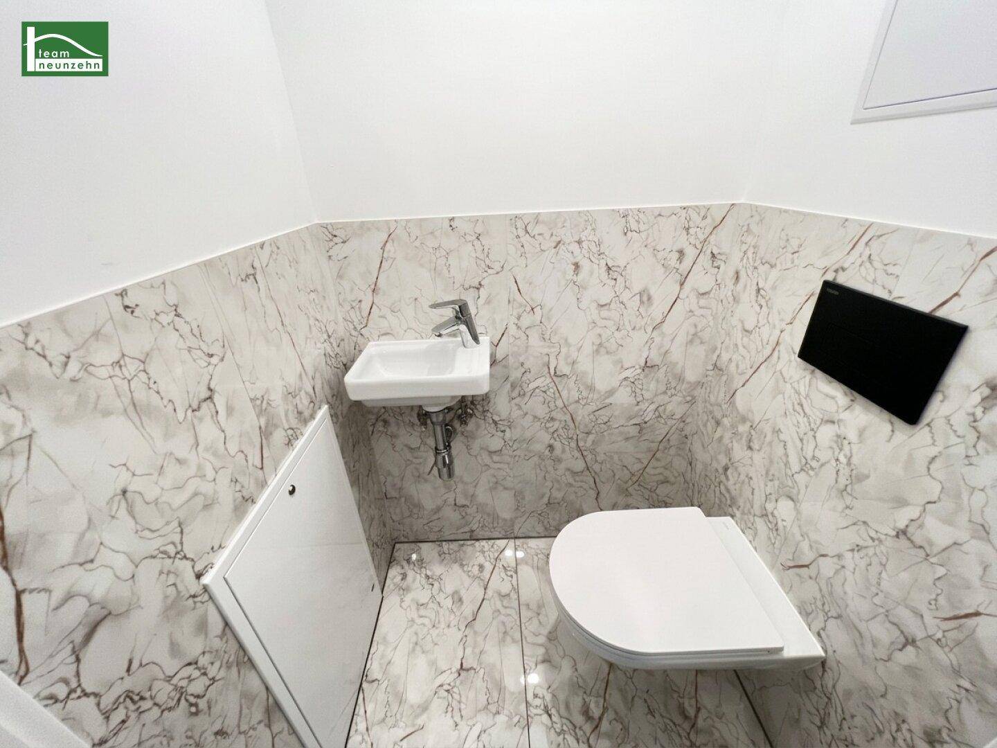 Separates WC mit Marmoroptik-Fliesen, wandhängendem WC und kleinem Handwaschbecken.