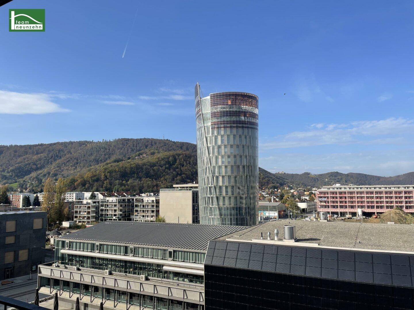 Panoramablick auf die Stadt mit moderner Architektur und umliegenden Hügeln.