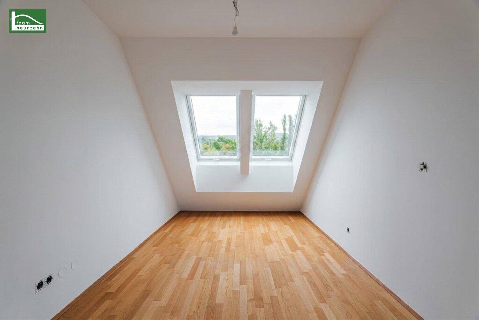 Leeres Dachzimmer mit zwei großen Dachfenstern und hellem Holzfußboden.