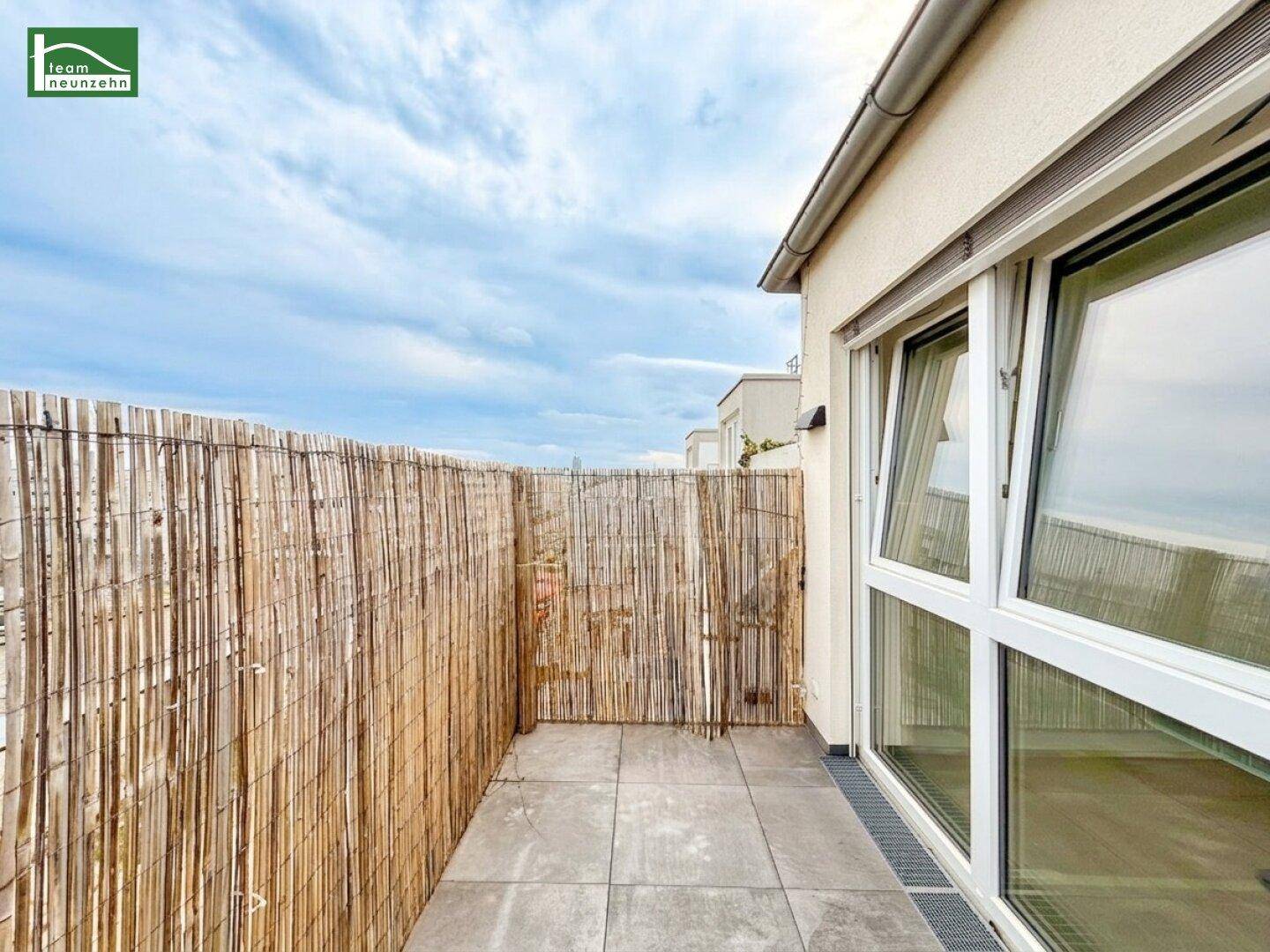 Heller Balkon mit Fliesenboden und Bambus-Sichtschutz, direkt zugänglich durch große Fenster.