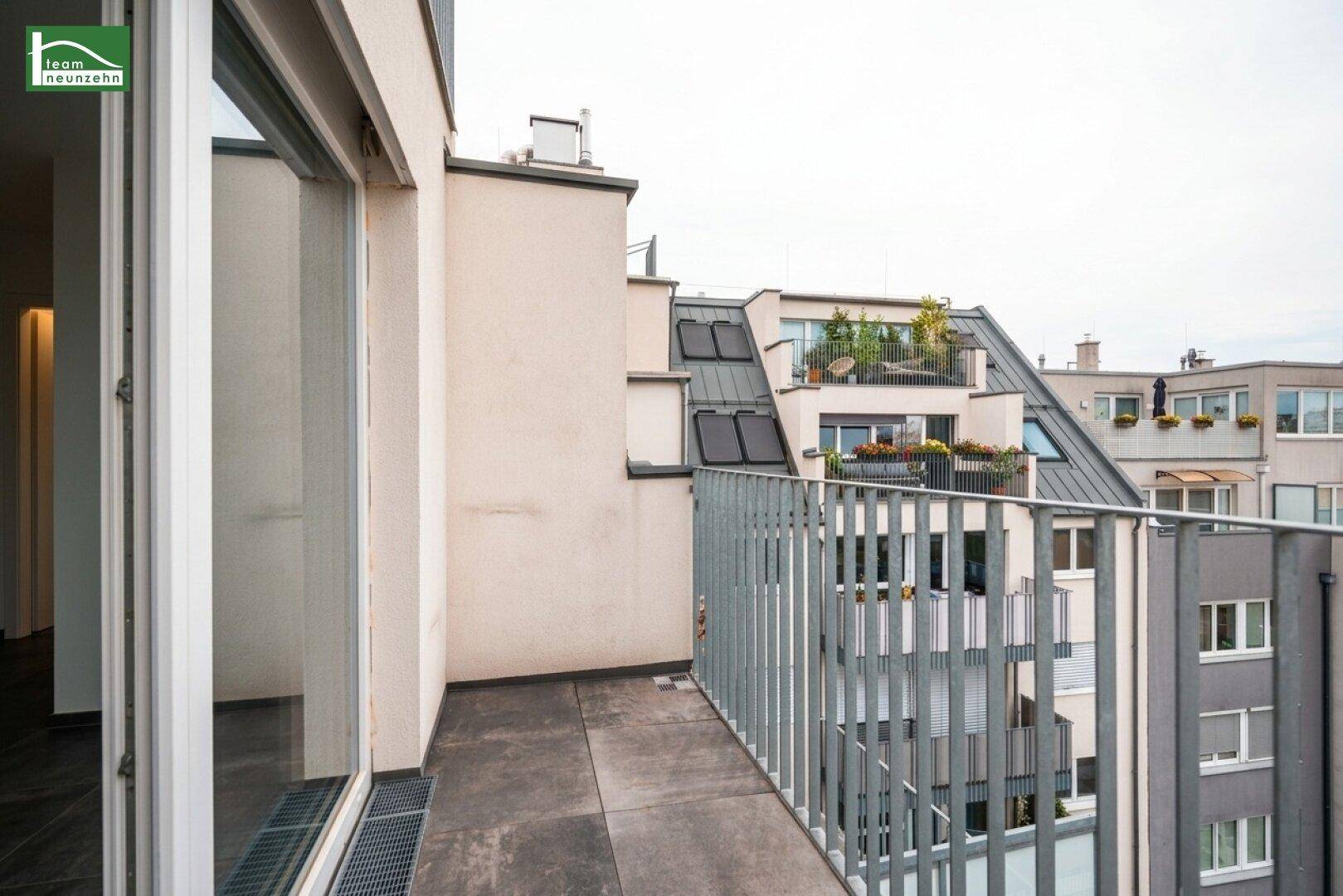 Geräumiger Balkon mit Metallgeländer und Blick auf umliegende Gebäude und Dächer.