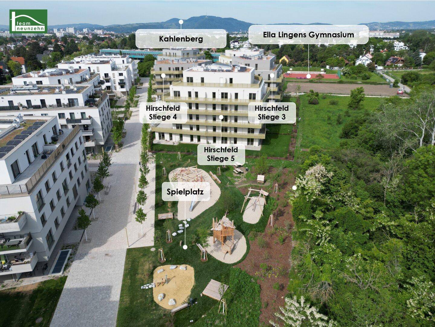 Luftaufnahme einer modernen Wohnanlage mit Spielplatz und viel Grünfläche, umgeben von Natur.