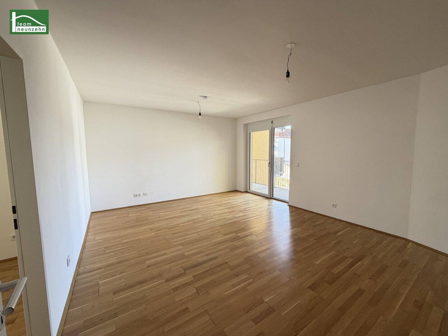 Helles, unmöbliertes Wohnzimmer mit Parkettboden und Zugang zum Balkon in einem Neubau.