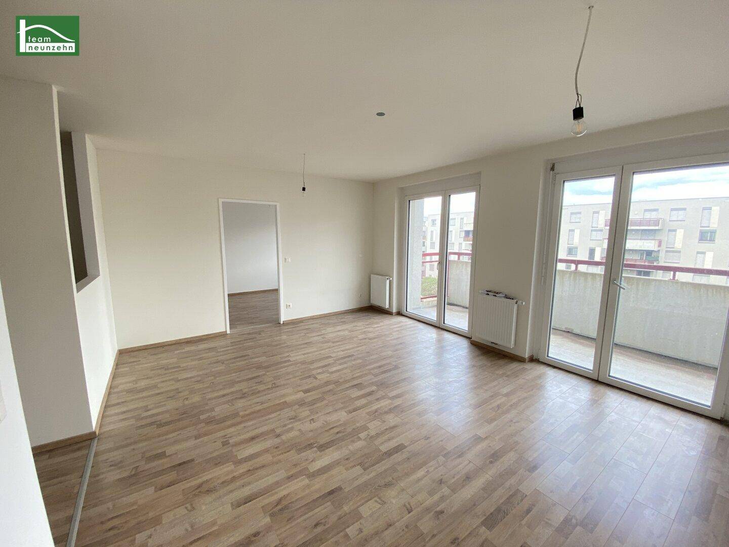 Heller Wohnbereich mit Laminatboden und großen Fenstertüren, die auf einen Balkon führen.