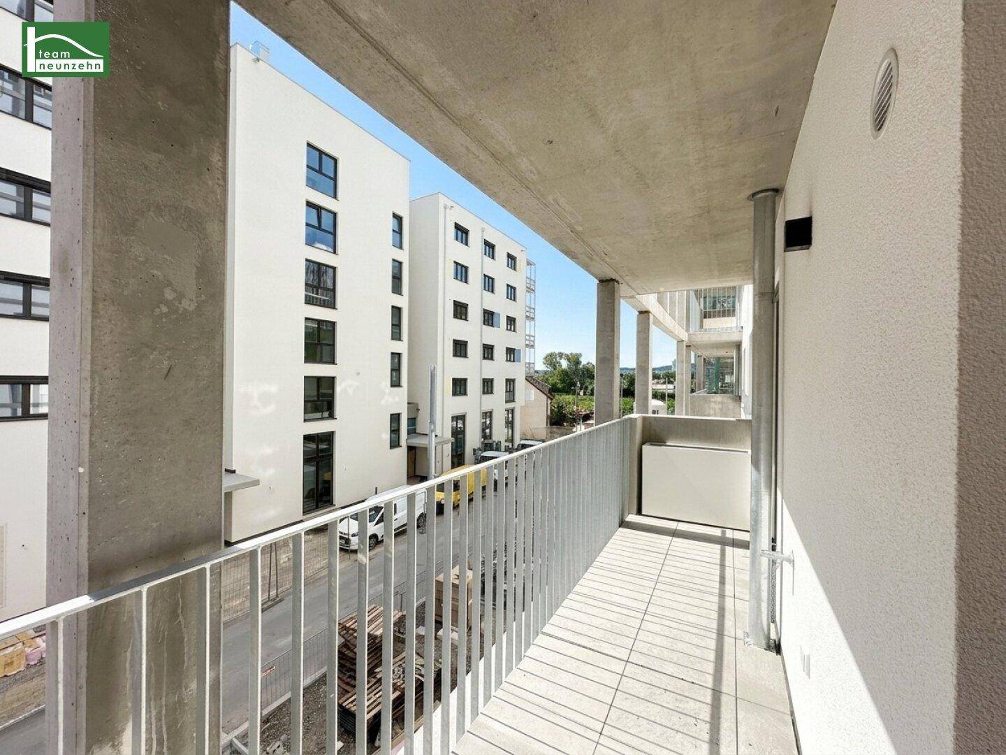 Langer, schmaler Balkon mit Fliesenboden und Blick auf moderne Wohngebäude.