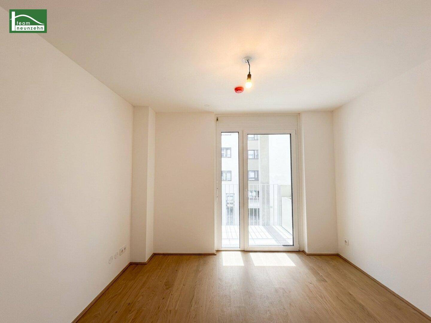 Helles Zimmer mit Holzboden und großem Fenster, ideal als Schlafzimmer oder Büro.