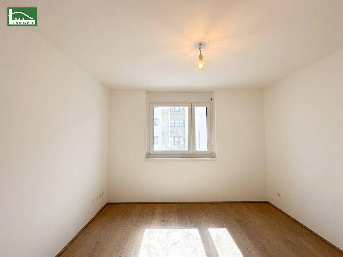 Leeres Zimmer mit Holzboden und Fenster, das viel Tageslicht hereinlässt.