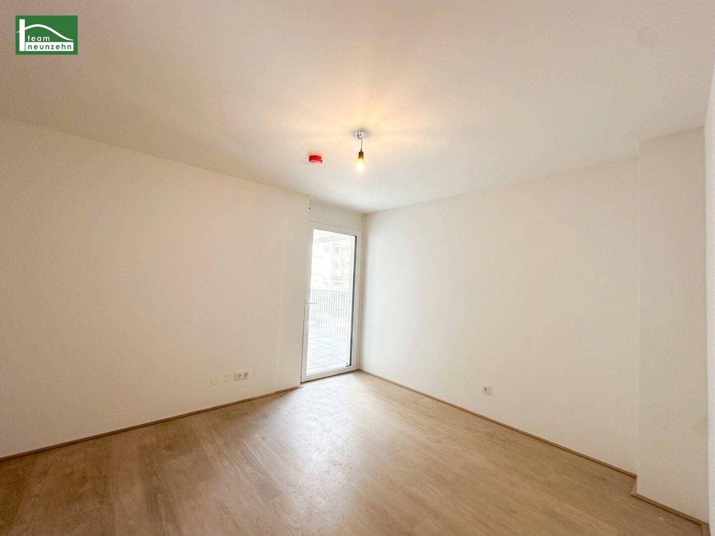 Helles, unmöbliertes Schlafzimmer mit Holzboden und Zugang zu einem kleinen Außenbereich.