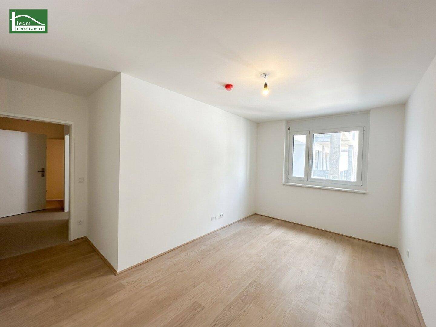 Unmöbliertes Schlafzimmer mit hellem Holzboden und einem Fenster zur Straße.