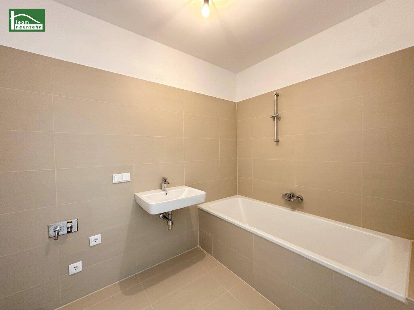 Modernes Badezimmer mit Badewanne, Waschbecken und beigefarbenen Fliesen.