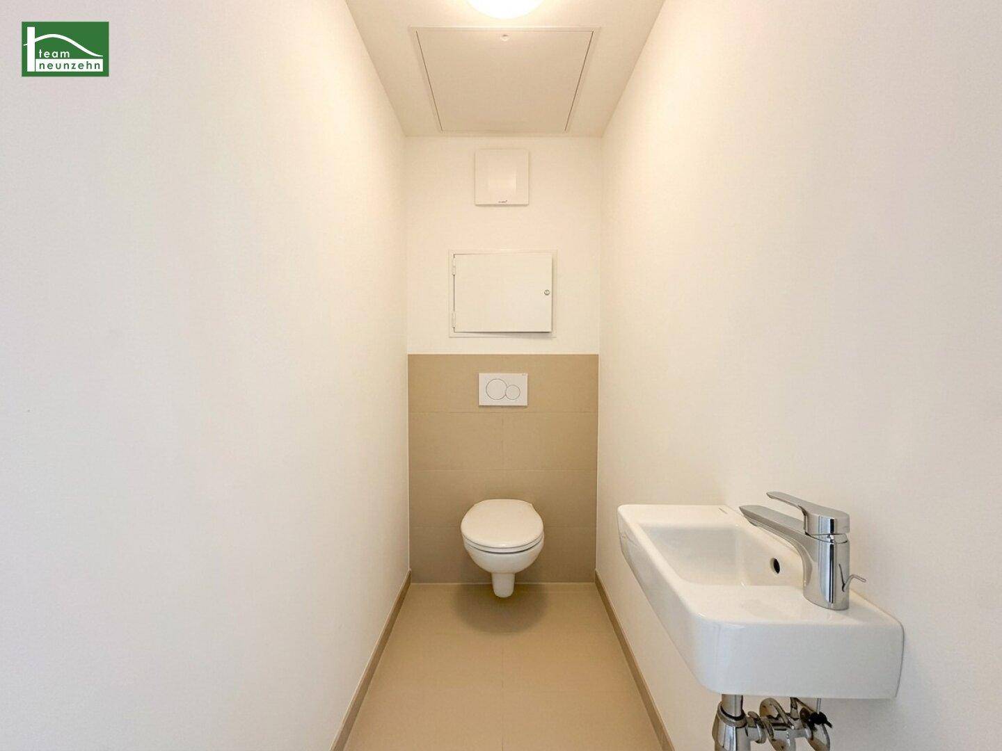 Gäste-WC mit wandhängender Toilette, kleinem Waschbecken und beigefarbenen Fliesen.