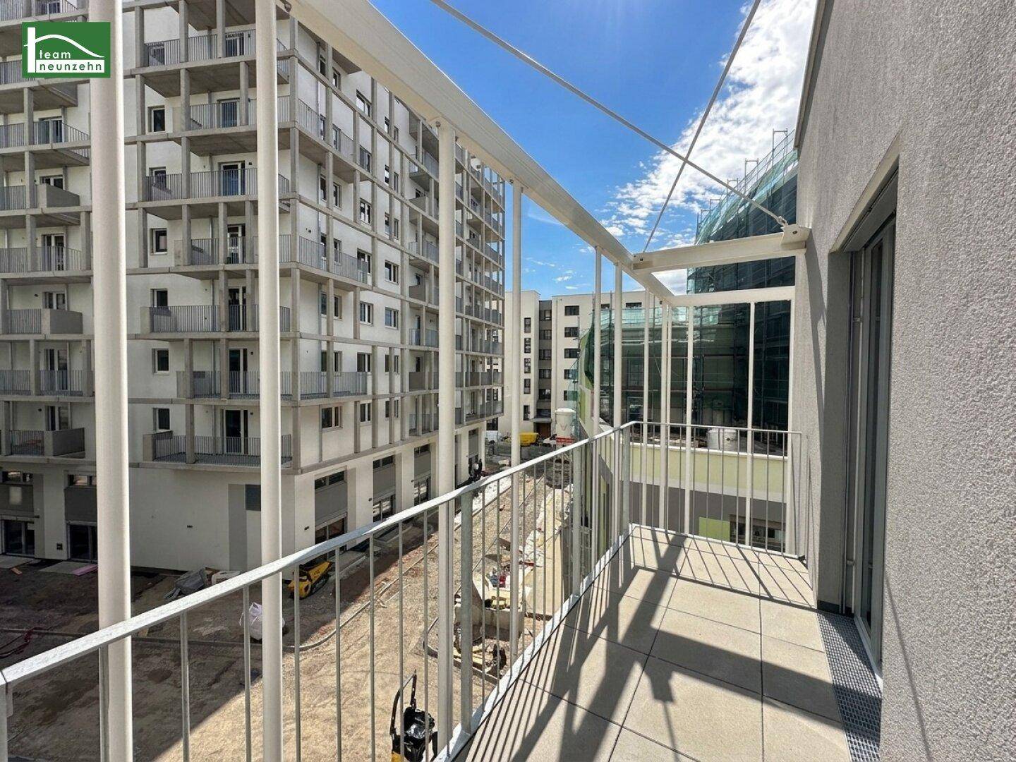 Balkon mit Fliesenboden und Metallgeländer, umgeben von modernen Wohngebäuden.