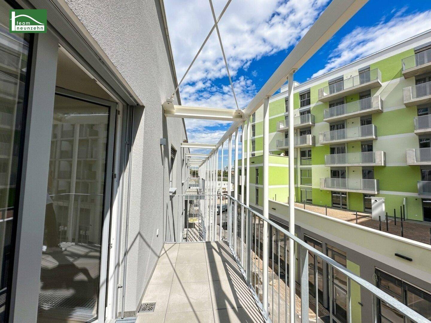 Langer Balkon mit Fliesenboden und Blick auf die umliegenden Neubauten.