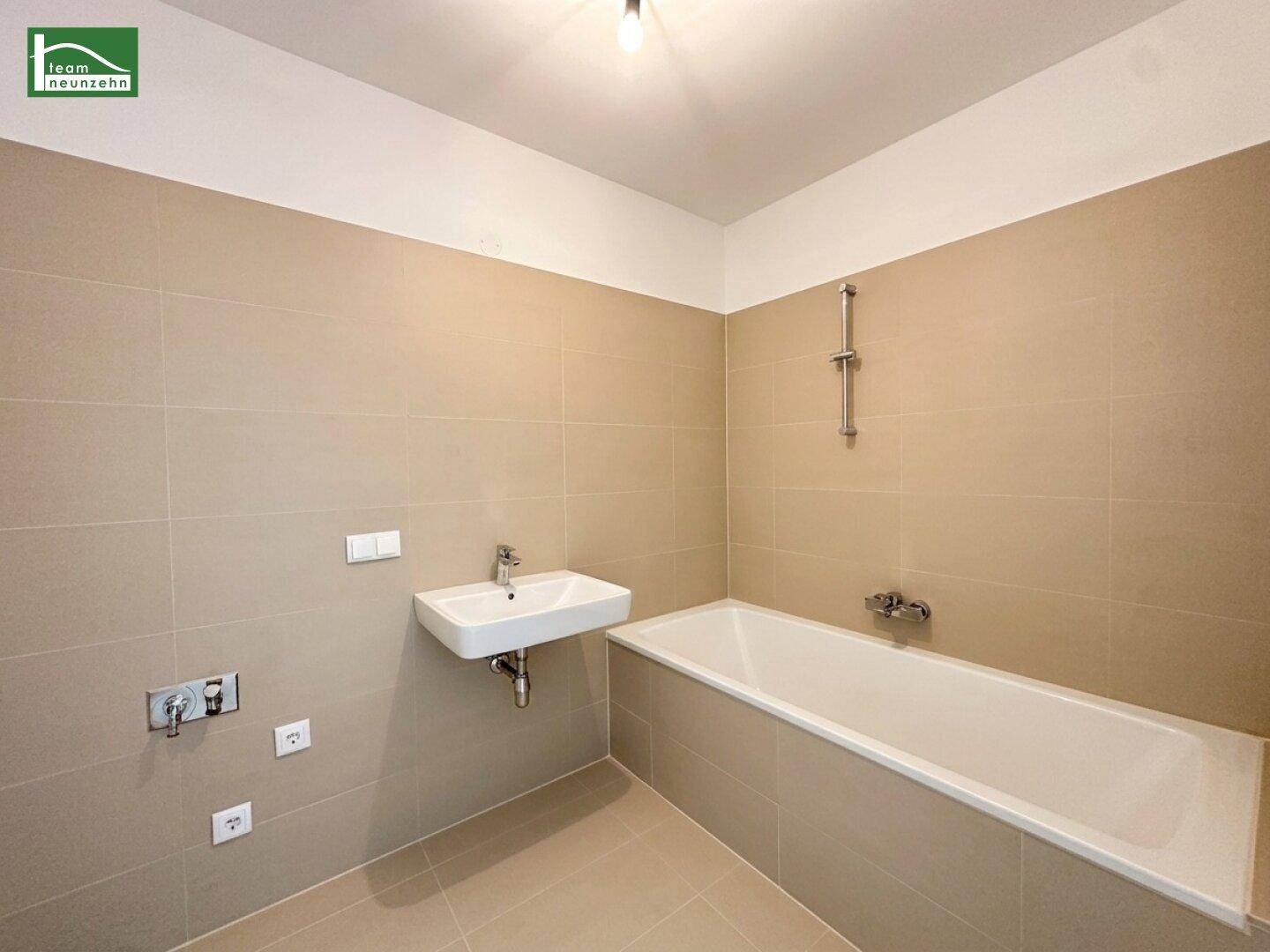 Modernes Badezimmer mit Badewanne, Waschbecken und beigefarbenen Fliesen.
