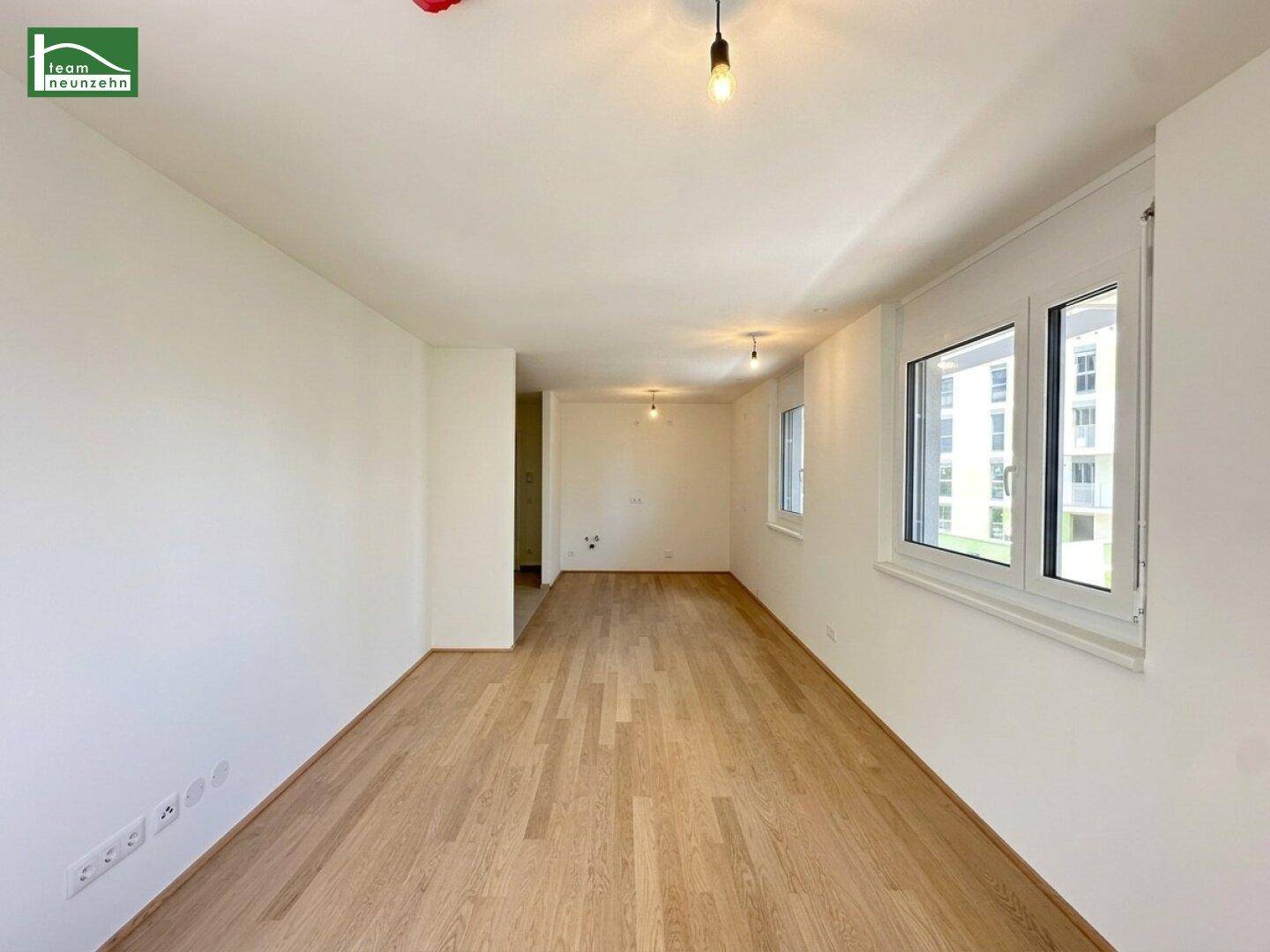 Geräumiges, unmöbliertes Zimmer mit hellem Parkettboden und großen Fenstern, ideal für Wohnzwecke.