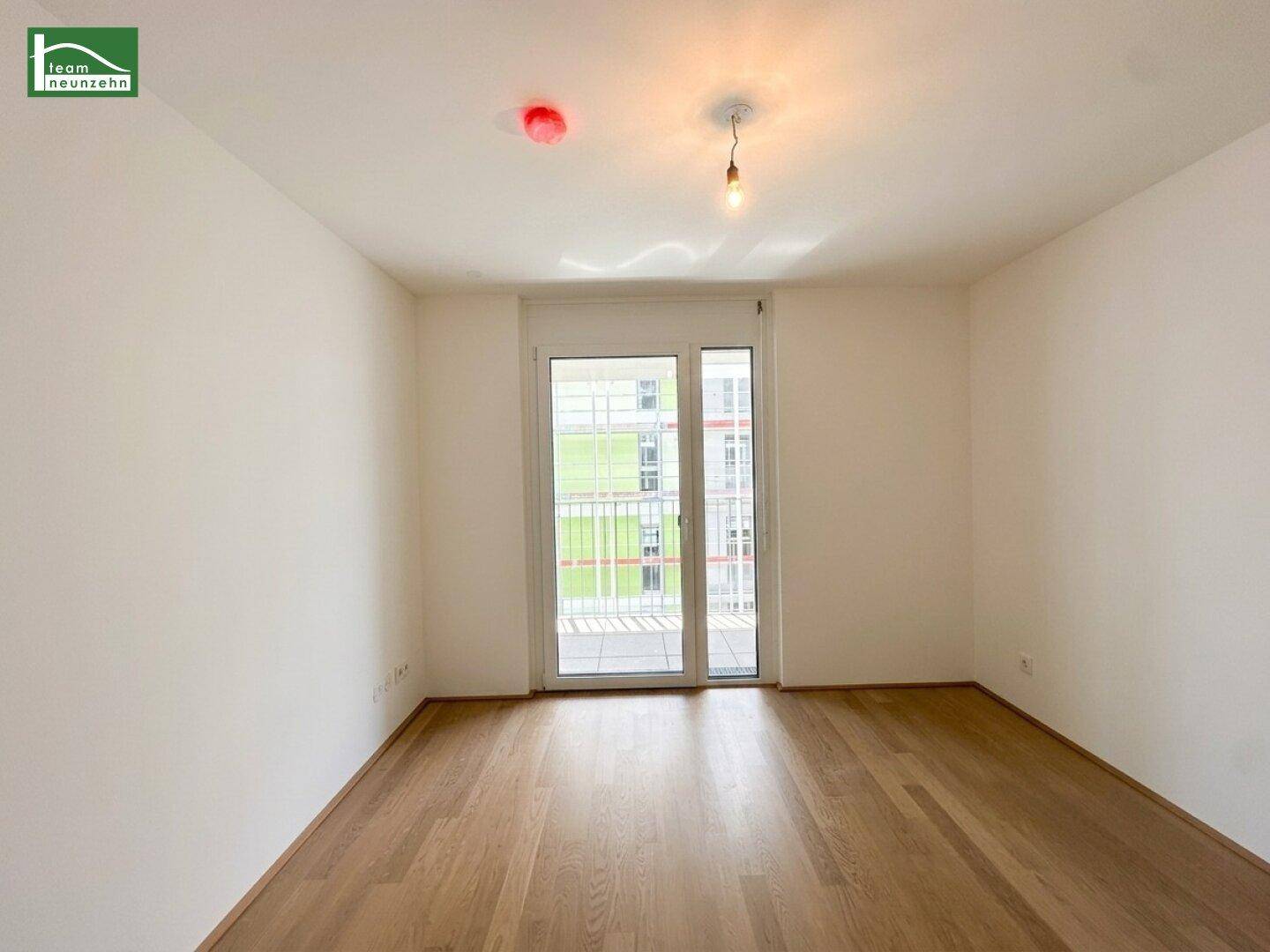 Helles Zimmer mit Parkettboden und großem Balkonzugang, bietet viel Tageslicht.