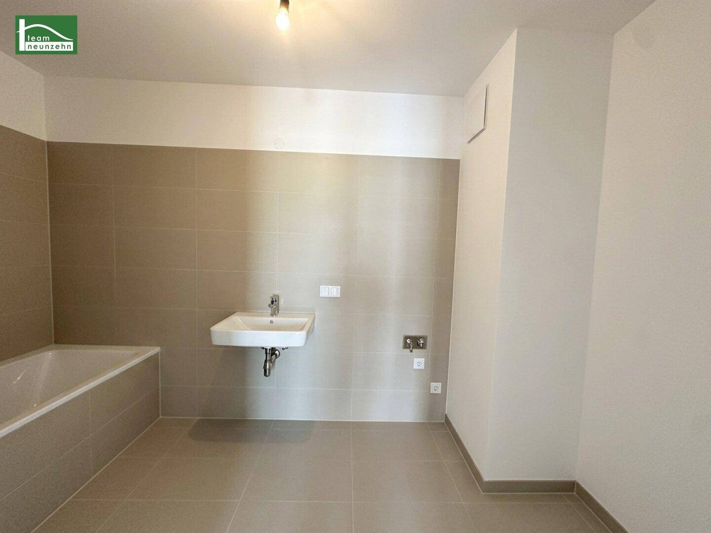 Modernes Badezimmer mit Badewanne, Waschbecken und beigefarbenen Fliesen an Wänden und Boden.