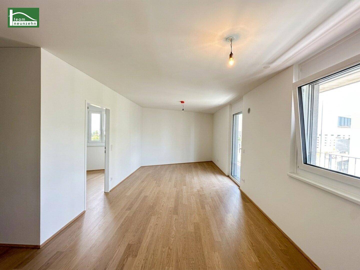 Geräumiges Wohnzimmer mit Holzboden und Blick auf den Außenbereich durch die Fenster.