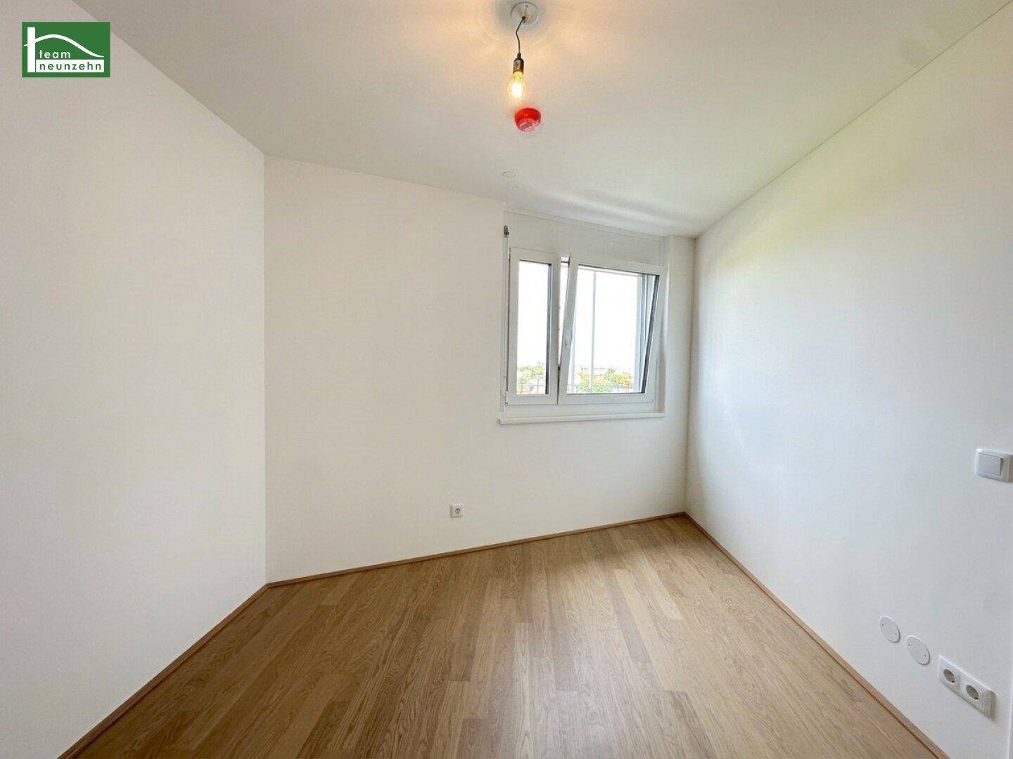 Helles Schlafzimmer mit Parkettboden und einem Fenster mit Rollladen.