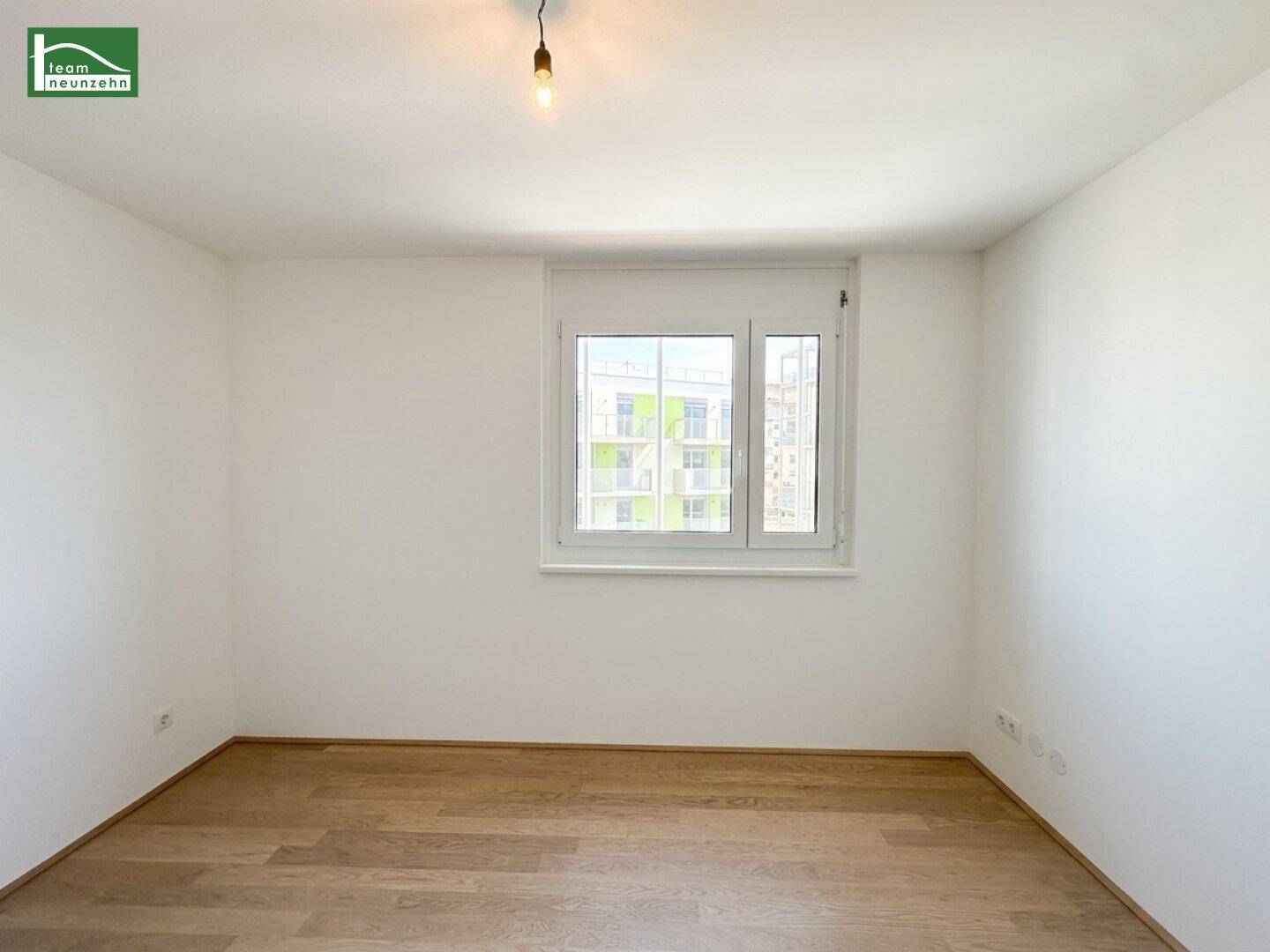 Leeres Schlafzimmer mit Parkettboden und großem Fenster.