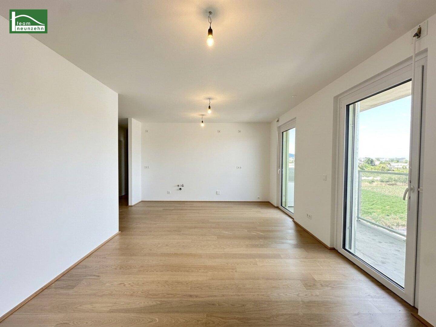 Geräumiges, helles Zimmer mit Holzboden und großem Fenster, das viel Tageslicht hereinlässt.