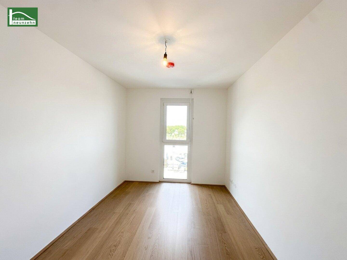 Freundliches Schlafzimmer mit Holzboden und einem großen Fenster, das für eine helle Atmosphäre sorgt.