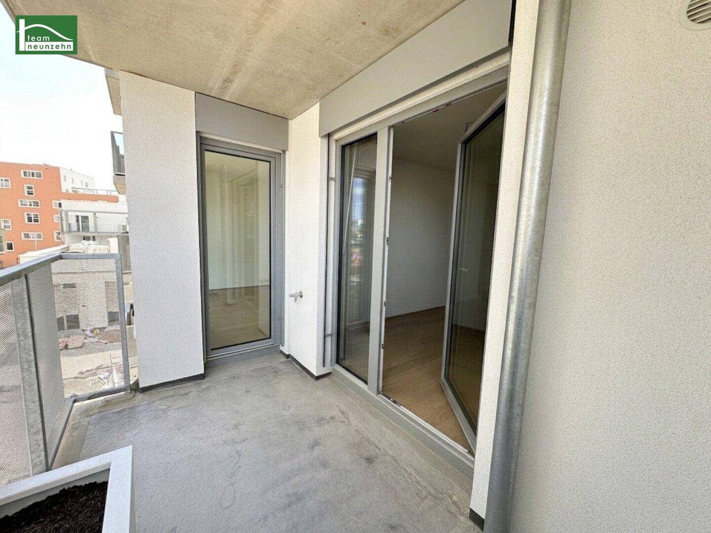 Balkon mit Glasgeländer und Zugang zu den hellen Innenräumen des Neubaus.