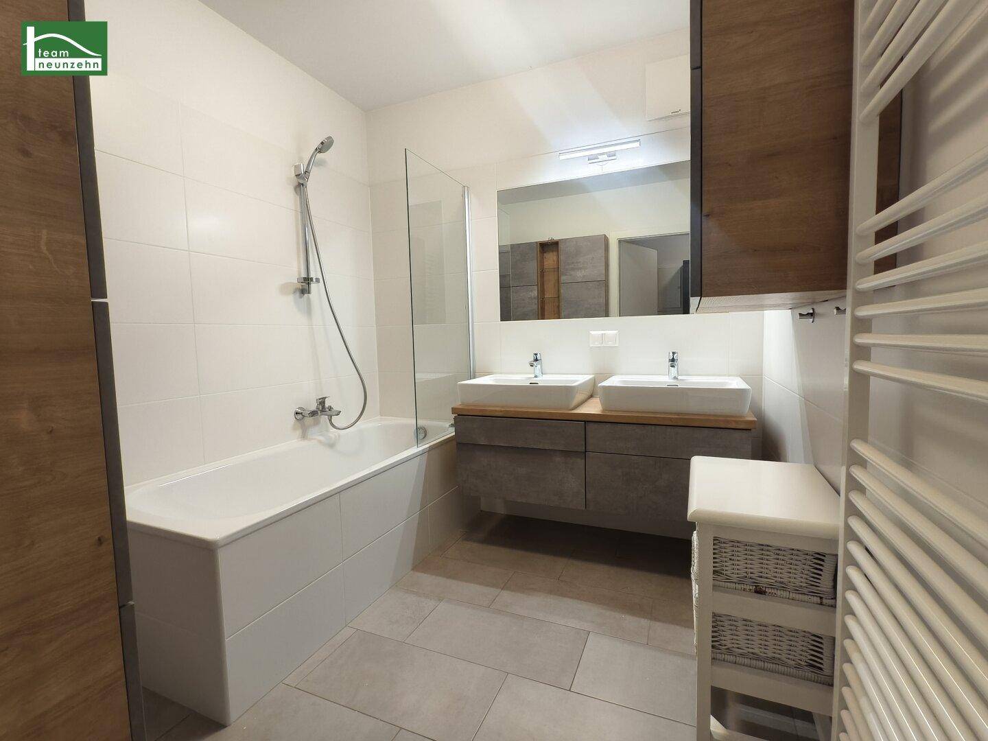 Modernes Badezimmer mit Doppelwaschbecken, Badewanne und hellen Fliesen.