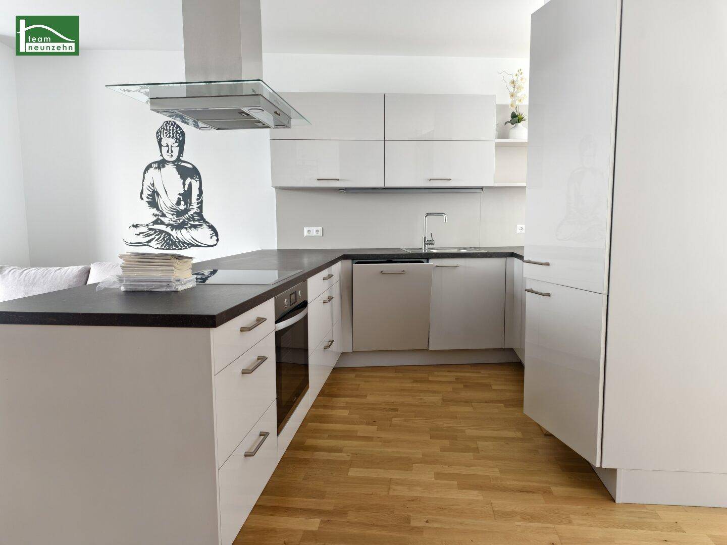 Moderne Küche mit weißen Hochglanzfronten, dunkler Arbeitsplatte und Holzboden.