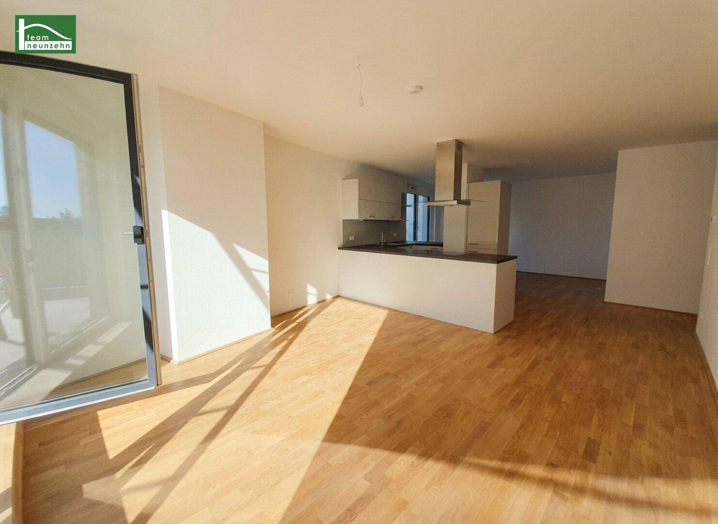 Heller offener Wohnbereich mit Holzboden, integrierter Küche und Zugang zu einem Balkon.