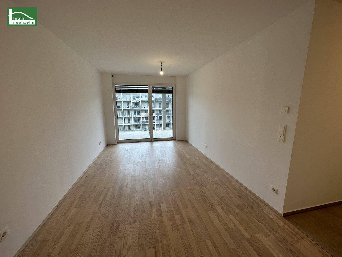 Heller Wohnraum mit Holzboden und großen Fenstern, die viel Tageslicht hereinlassen.