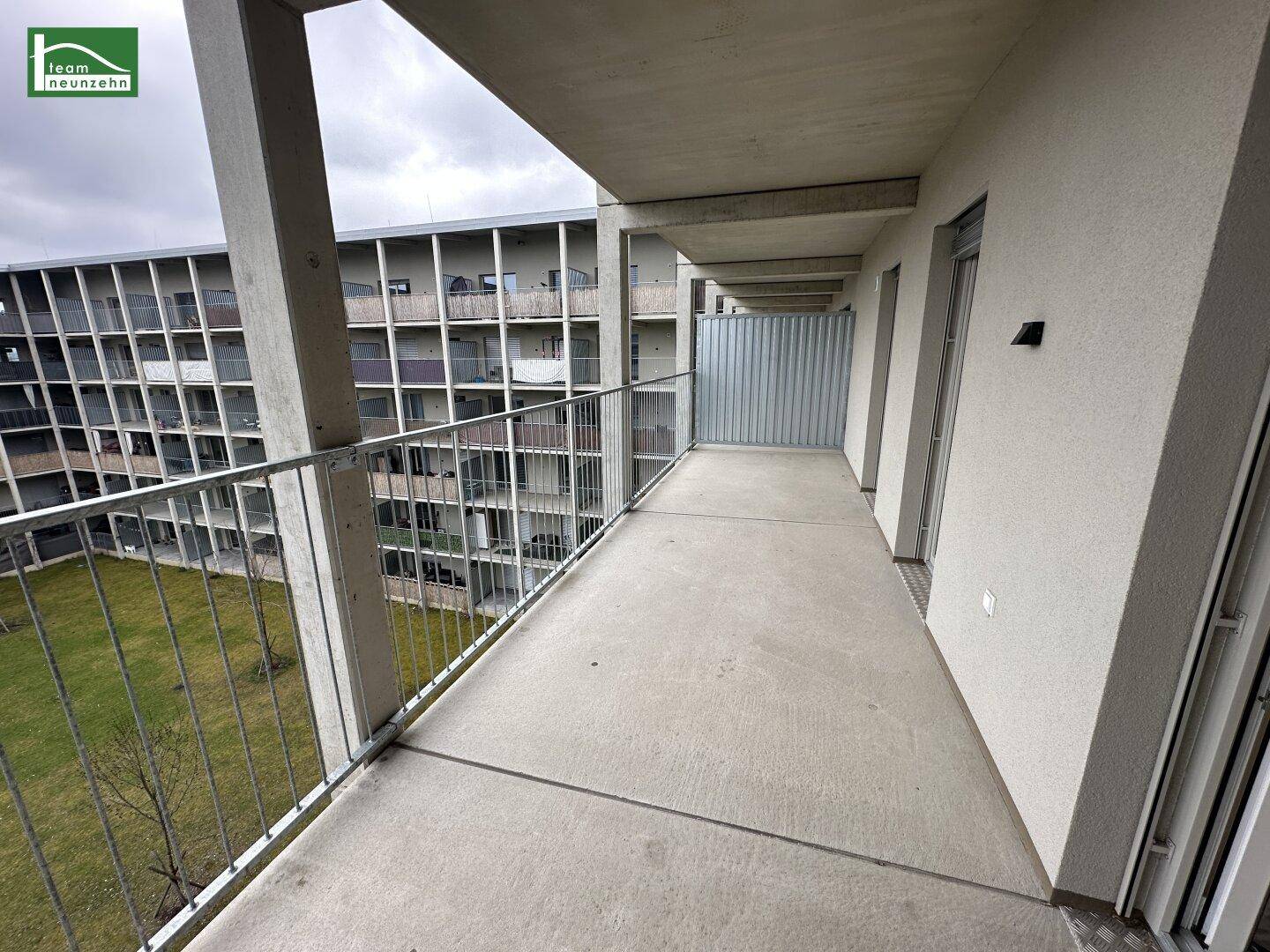 Langer Balkon mit Metallgeländer und Blick auf den Innenhof der Wohnanlage.