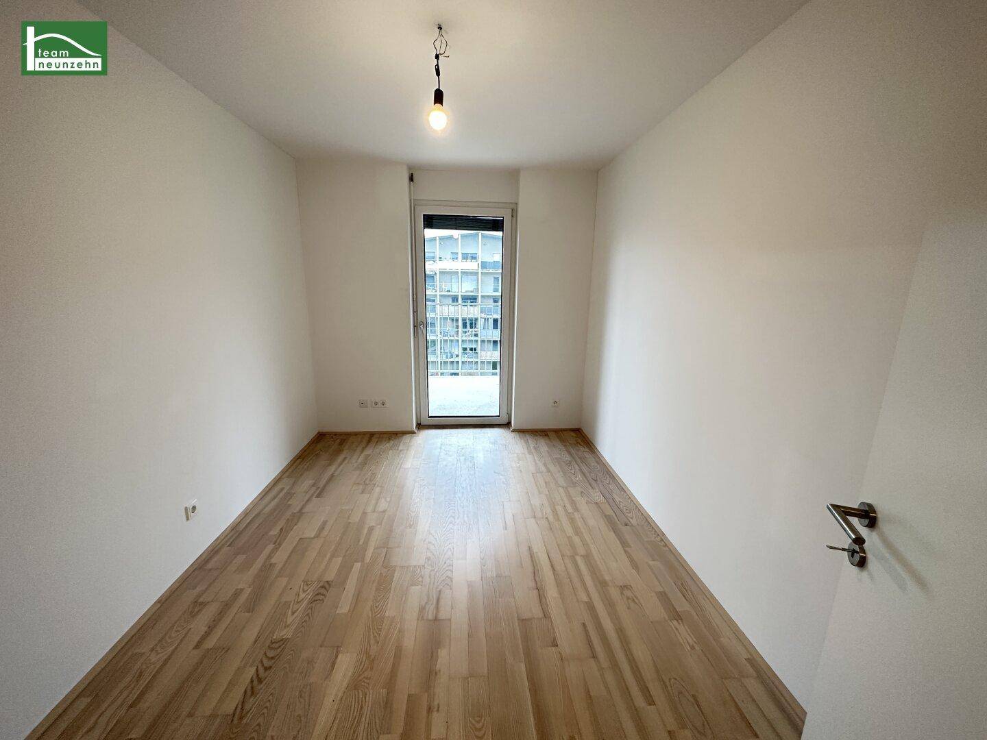 Leeres Zimmer mit Holzboden und Zugang zu einem französischen Balkon oder kleiner Loggia.