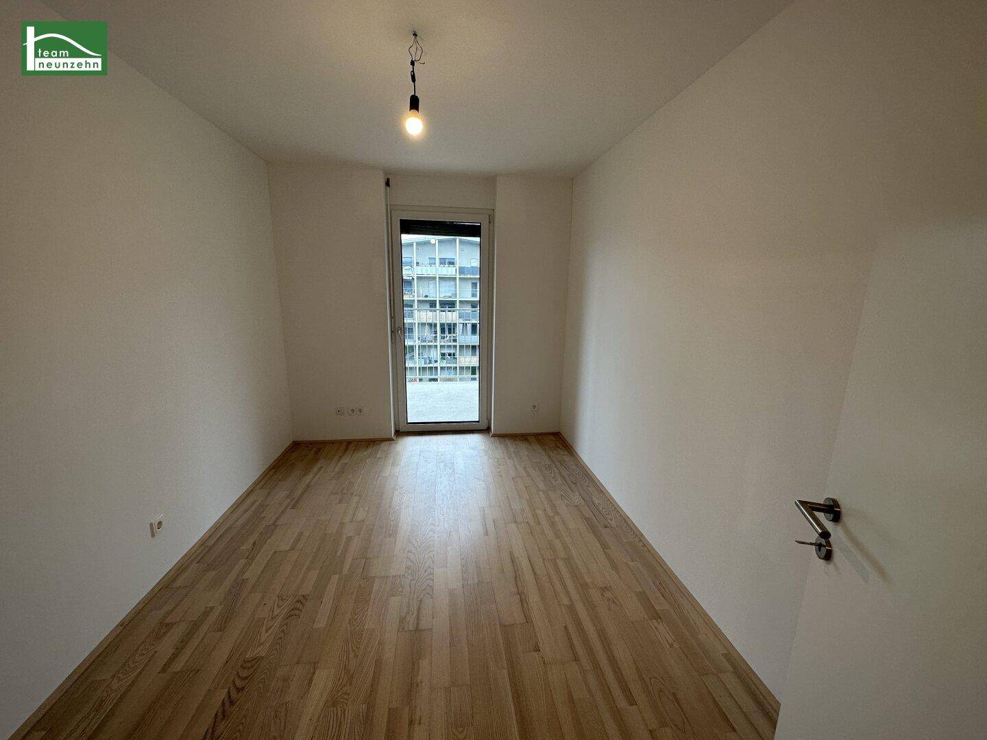 Leeres Schlafzimmer mit hellem Holzboden und Zugang zu einem Außenbereich.