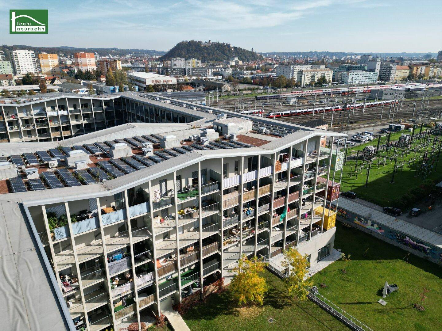 Luftaufnahme eines modernen Wohnkomplexes mit vielen Balkonen, Grünflächen und Photovoltaikanlage.