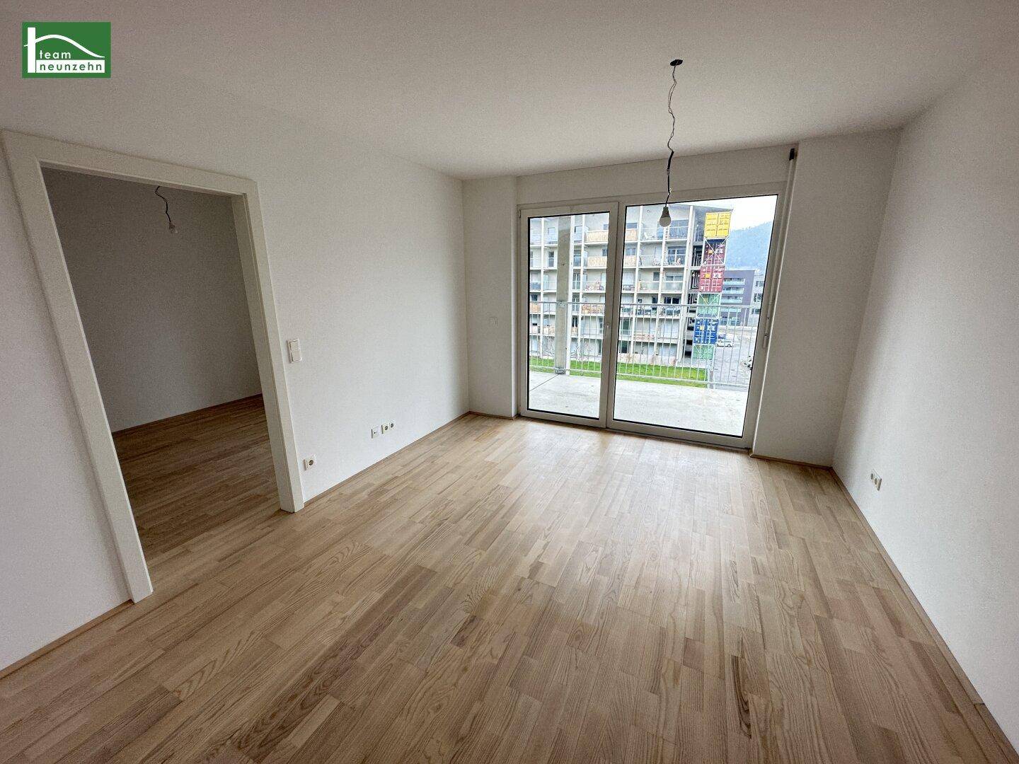 Leeres Wohnzimmer mit Holzboden und großem Fenster, bereit zur individuellen Gestaltung.