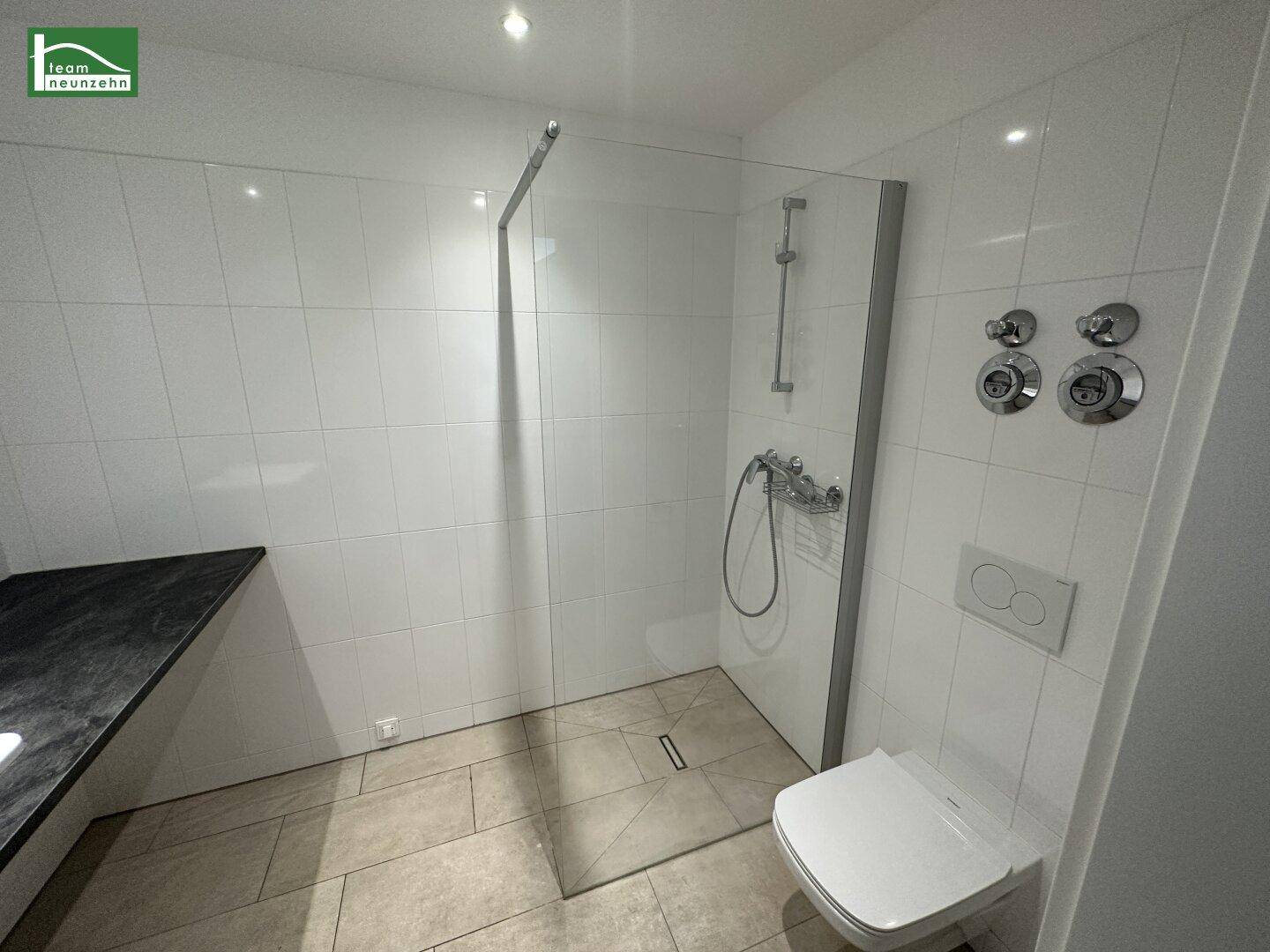 Modernes Badezimmer mit ebenerdiger Dusche, Glasabtrennung und wandhängendem WC.