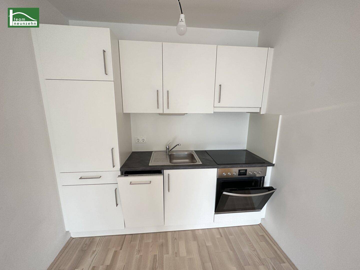 Kleine, moderne Einbauküche mit weißen Schränken, dunkler Arbeitsplatte und integriertem Backofen.