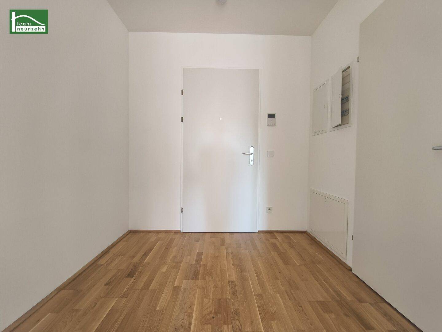 Eingangsbereich mit hellem Parkettboden und weißer Eingangstür, die in die Wohnung führt.