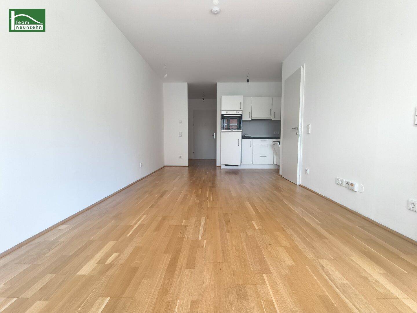 Heller Wohnbereich mit Parkettboden und integrierter Küchenzeile, ideal für offenes Wohnen.