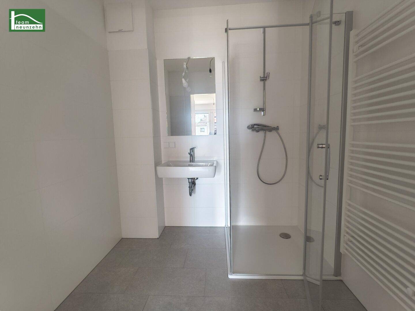 Modernes Badezimmer mit Duschkabine, Waschbecken und beheiztem Handtuchhalter.
