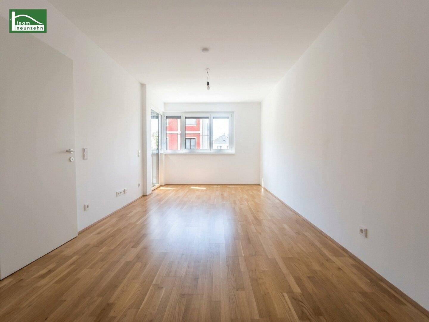 Lichtdurchfluteter Wohnraum mit hellem Parkettboden und Zugang zu einem Balkon.