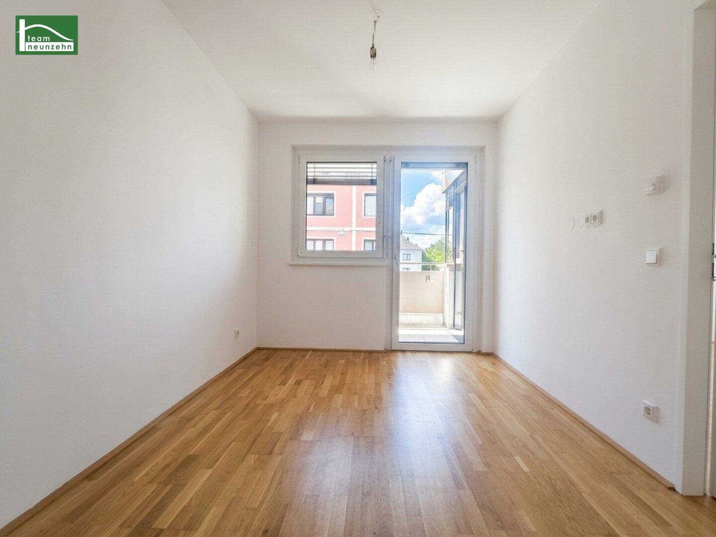 Helles Zimmer mit Parkettboden und großem Fenster, das viel Tageslicht hereinlässt.