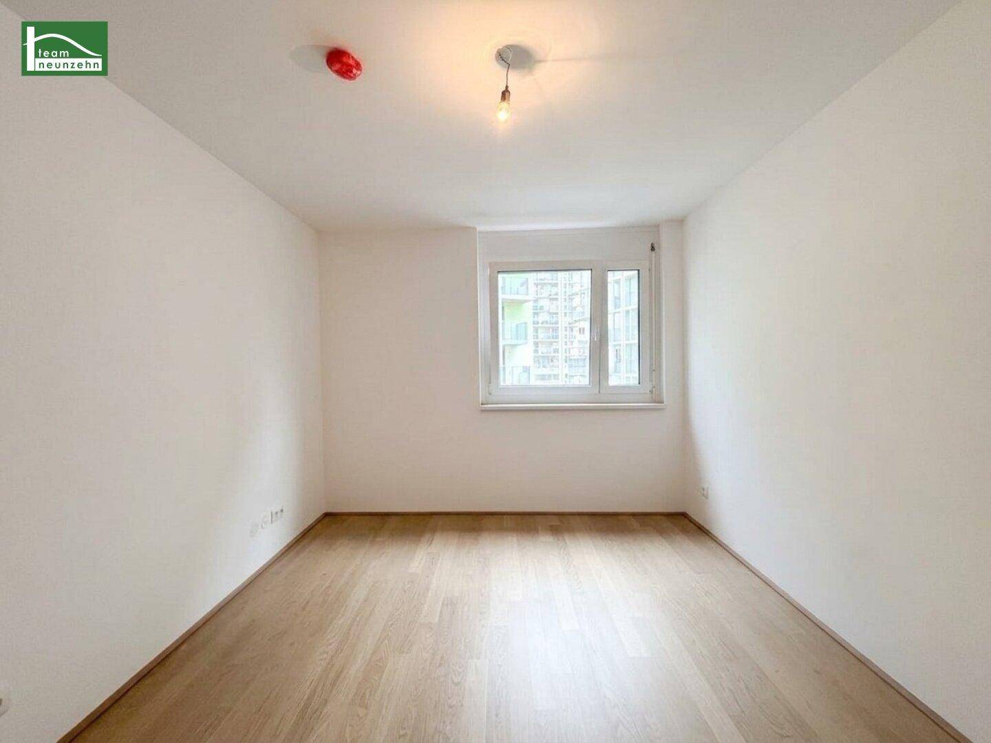 Helles, leeres Zimmer mit Holzboden und einem Fenster, ideal als Schlafzimmer.