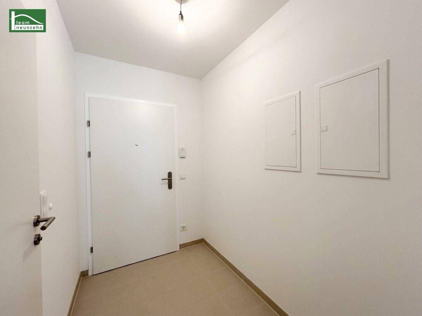 Heller Eingangsbereich mit weißer Tür und Fliesenboden in einem Neubau.